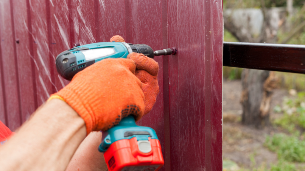 A man drilling a hole in a fence with a power drill.