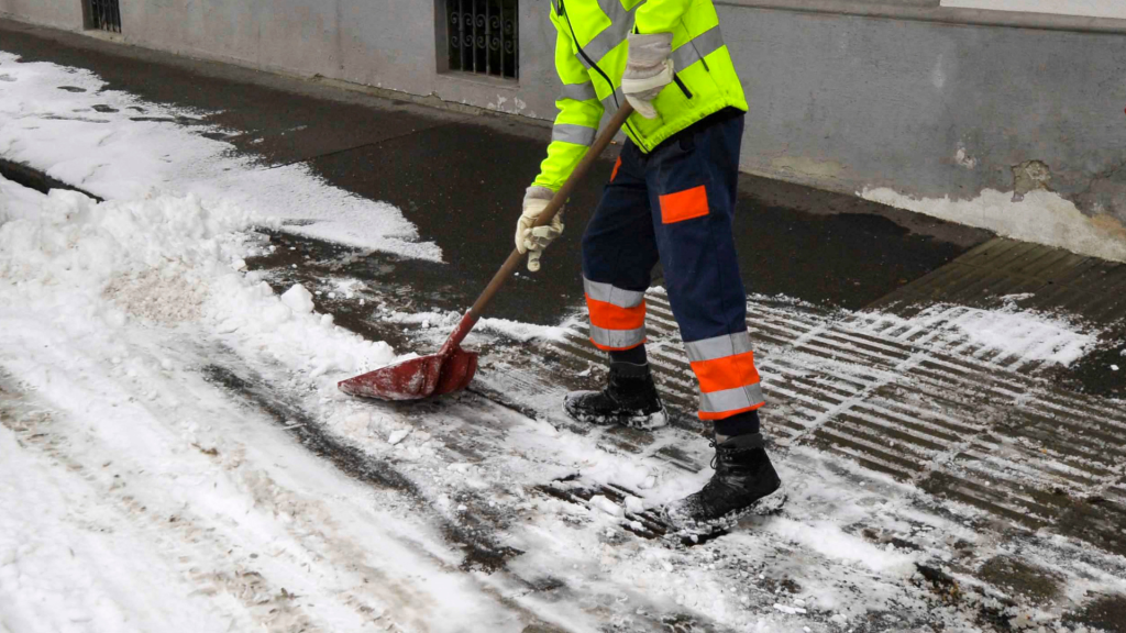 A man in a yellow safety vest shoveling snow from the street during winter.